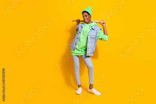 Full length body size view of attractive cheerful girl holding bat posing isolated over bright yellow color background