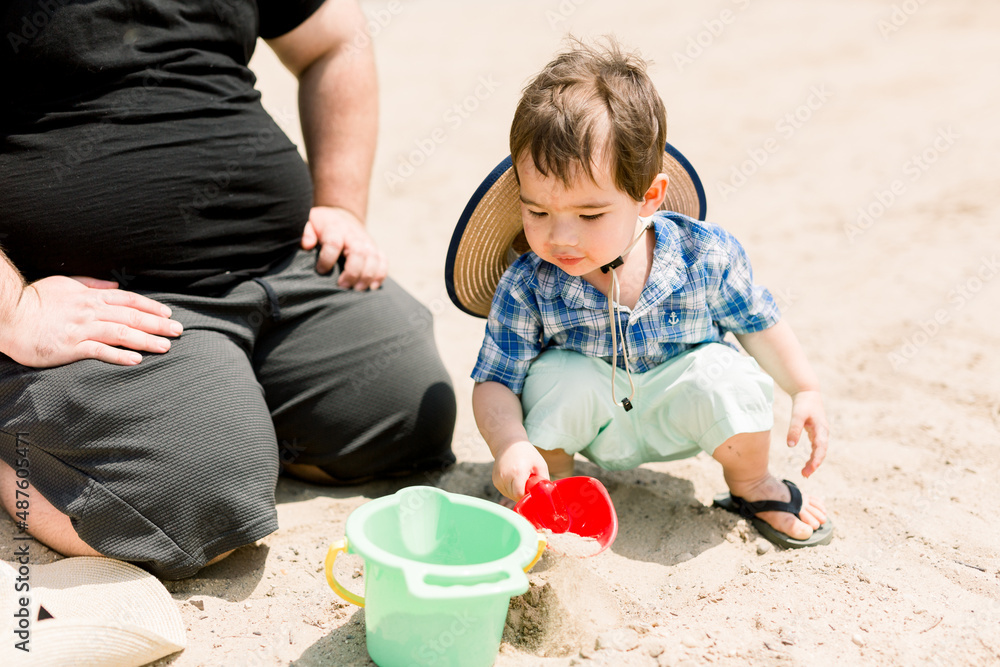 Naklejka premium Little Boy is Playing at the Beach with Bucket and Shovel at the Beach