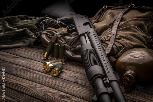 A black 12-gauge pump-action shotgun and ammo are on a canvas backpack. A smooth-bore weapon with a plastic stock. Dark back