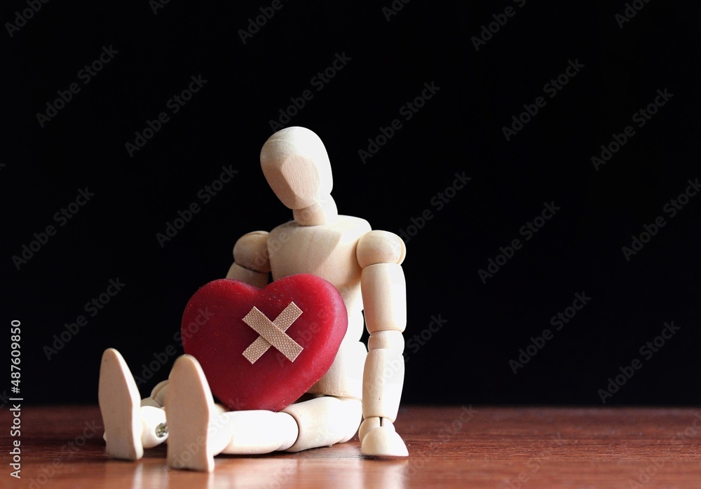 Sad, heartbroken and lonely concept. Wooden doll sit in the dark with red heart and bandage. Sad, heartbroken and lonely concept. Wooden doll sit in the dark with red heart and bandage.