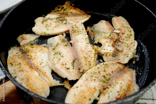 Fresh Tilapia Frying in a Black Pan with Butter and Herbs
