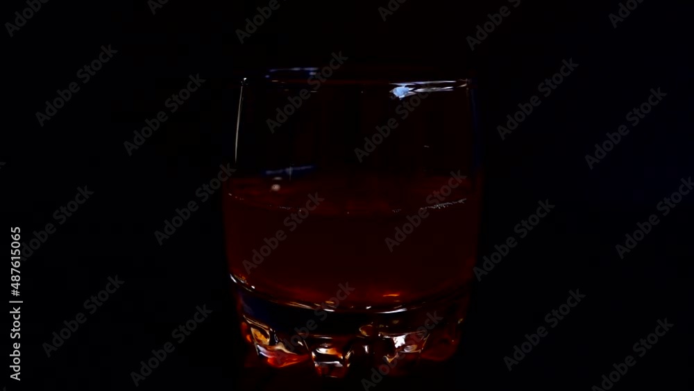 Falling ice cubes into a whiskey glass on an isolated black background. Slow motion. Falling ice cubes into a whiskey glass on an isolated black background. Slow motion.