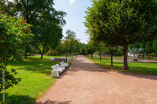 A deserted park without people with white benches and a fountain. Summer. Day