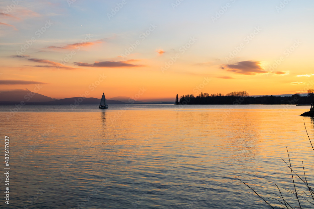 Petit voilier sur le Lac Léman au coucher du soleil depuis les berges à Morges (Canton de Vaud, Suisse)