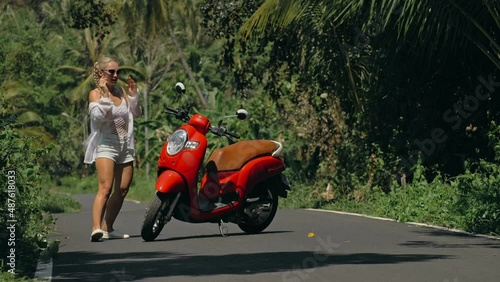 Woman on red scooter in white clothes drive on forest road trail. Dancing trip. One girl caucasian tourist in sunglasses dance, relax, rest near motorbike. Asia Thailand ride tourism. Motorcycle rent.