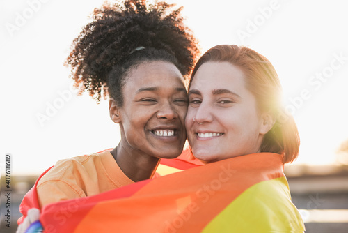 Mulitracial lesbian couple hugging together outdoor with sunset in background - LGBTQIA concept photo