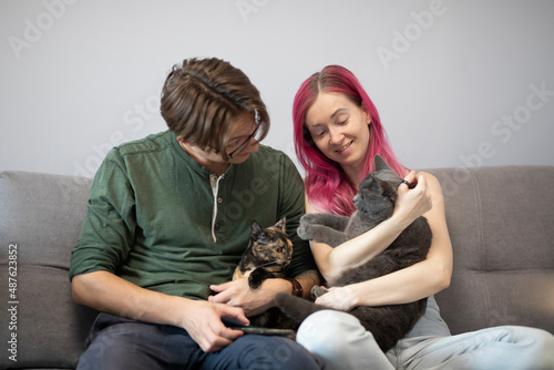 a man and a woman sit on a gray sofa and hug cats