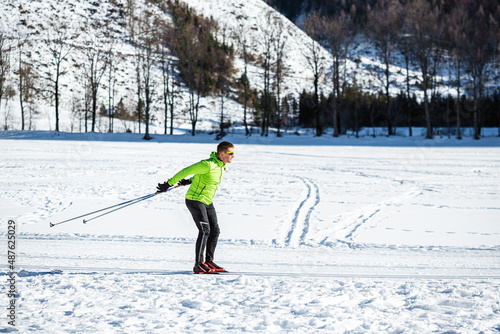 Mature man cross country skiing, on the ski trail surrounded by mountains and forest.
