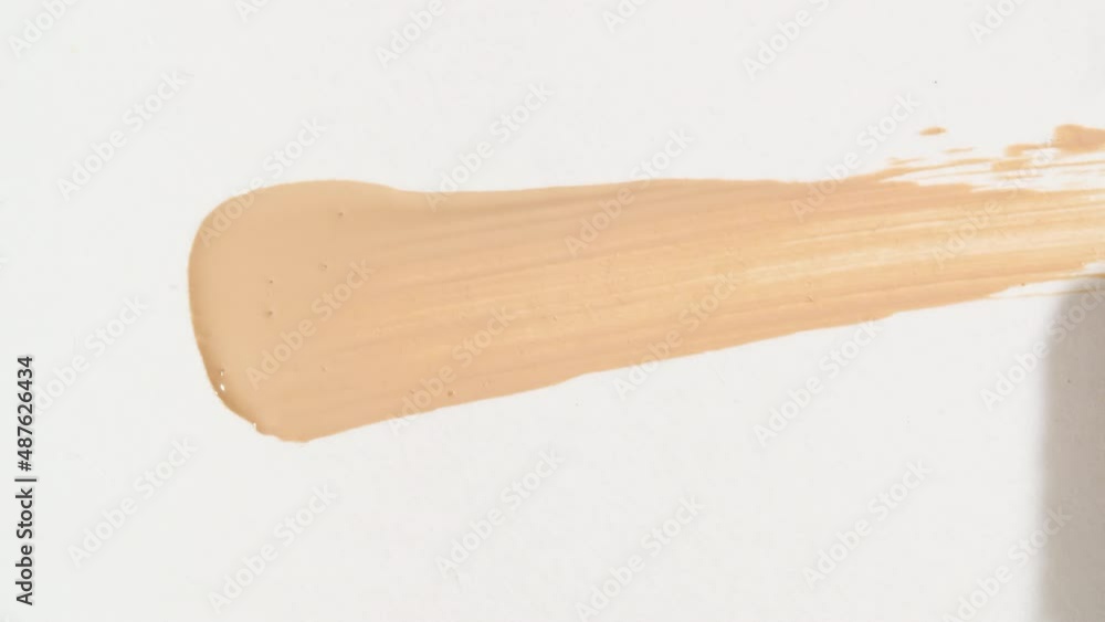 Macro shot and slow motion of a brush, applicator, smear, concealer isolated on white background. Advertising professional cosmetics. Closeup of a cosmetic liquid foundation or cream beige color. 4k Macro shot and slow motion of a brush, applicator, smear, concealer isolated on white background. Advertising professional cosmetics. Closeup of a cosmetic liquid foundation or cream beige color. 4k
