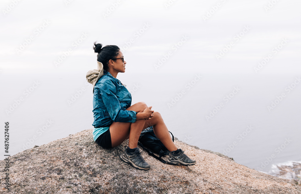 Woman hiker relaxing on a rock. Female mountain climber in sports clothes and sunglasses looking at the view.