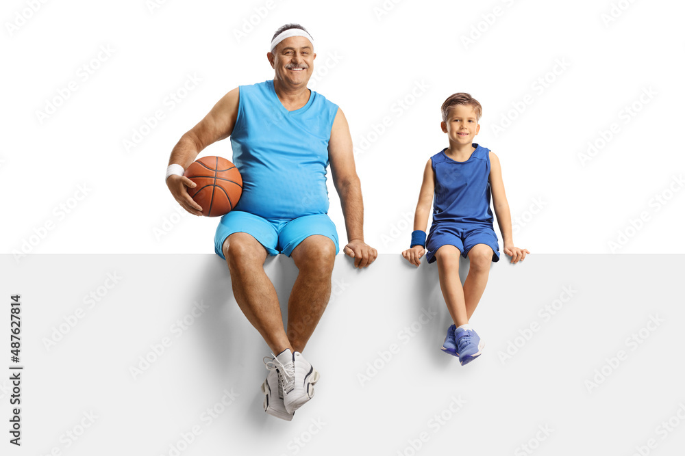 Mature man with a basketball and a boy in sport jersey sitting on a blank panel Mature man with a basketball and a boy in sport jersey sitting on a blank panel