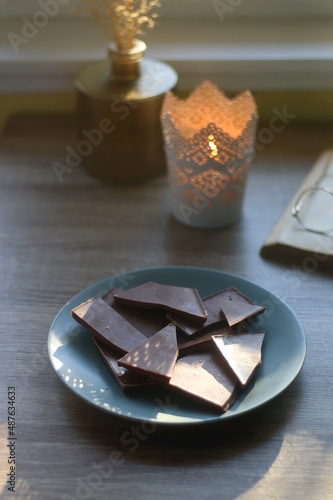 Plate of chocolate, open book, reading glasses, lit candle and flowers on the table. Selective focus.