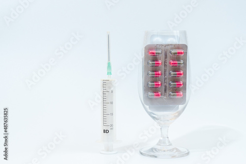 Tablets and medical capsules in glass with syringe isolated on white background