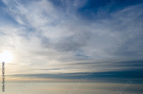 Aerial view of bright yellow sunset over white dense clouds with blue sky overhead.