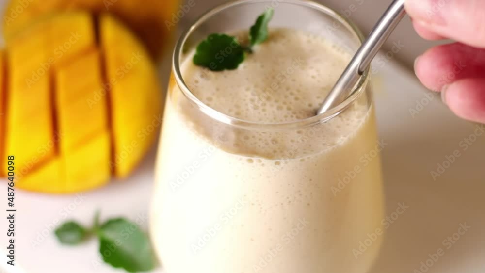 A metal drinking straw is placed in a glass of Indian drink lassie. Milk, mango, yogurt, mint.
