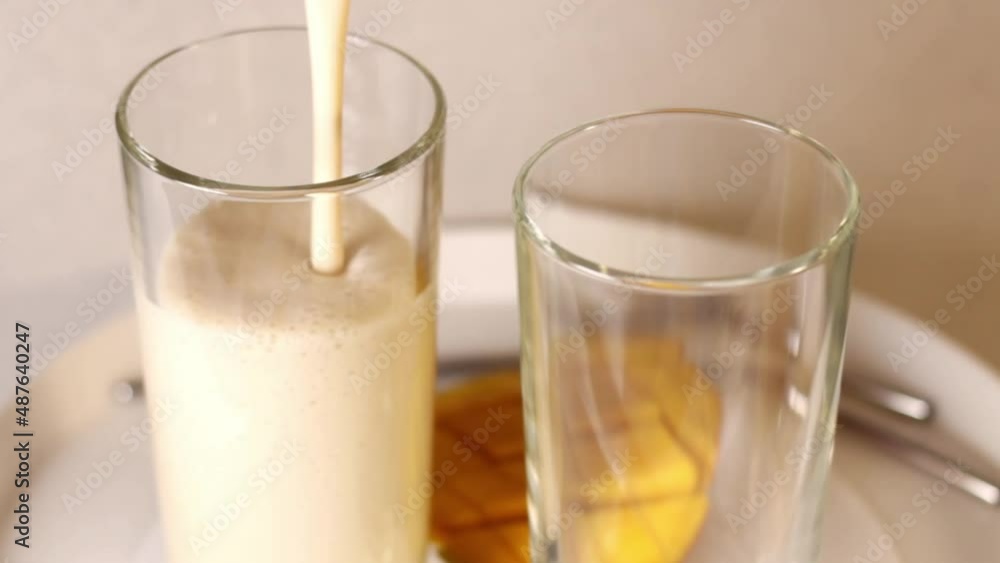 Lassie, a traditional Indian drink, is poured into a glass. In the background are mangoes, metal reusable drinking straws. Lassie, a traditional Indian drink, is poured into a glass. In the background are mangoes, metal reusable drinking straws.