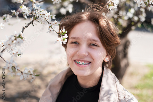 Young teen girl with a charming smile near a flowering tree in spring  the girl is happy that she has braces on her teeth  orthodontic concept. Focus on the teeth and braces of the girl