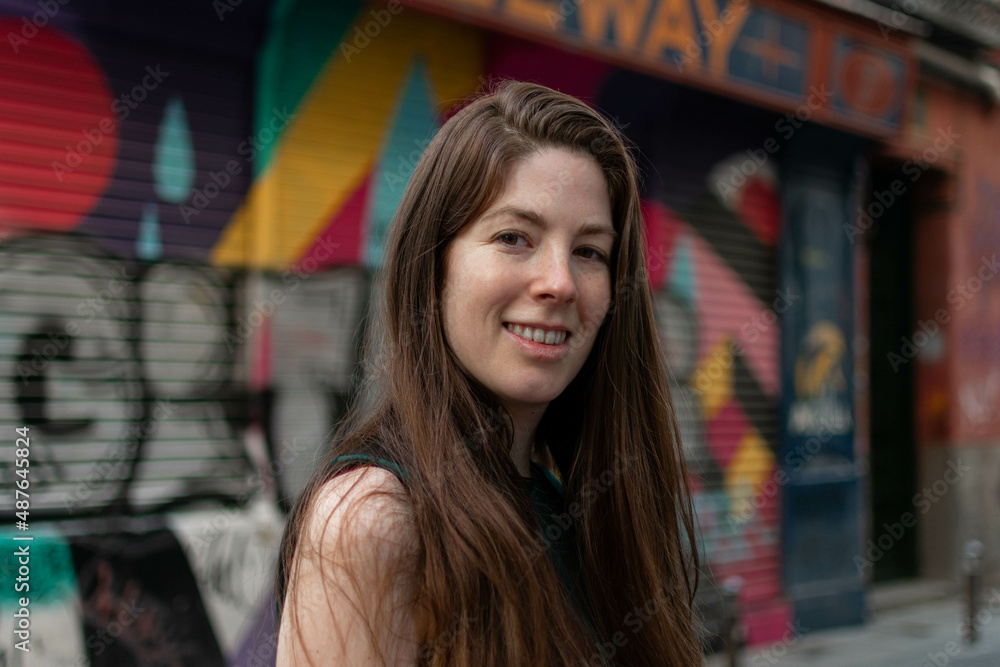 Close-up portrait of young smiling woman knitted hat posing against wall painted with graffiti. Urban clothing style, urban background. Close-up portrait of young smiling woman knitted hat posing against wall painted with graffiti. Urban clothing style, urban background.