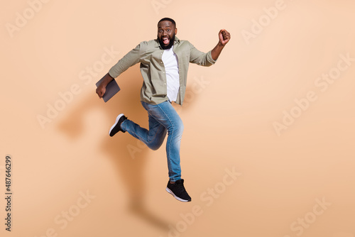 Full body profile photo of impressed young beard guy run hold laptop wear shirt jeans footwear isolated on beige background