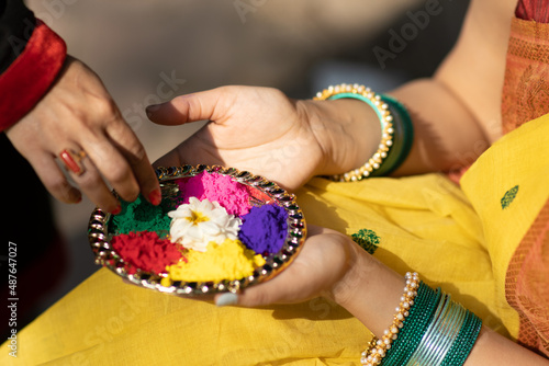 Hands of two Beautiful young woman or girl holding color or colour or gulal or abeer or Holi powder arranged in a decorated plate to celebrate holi festival of colors