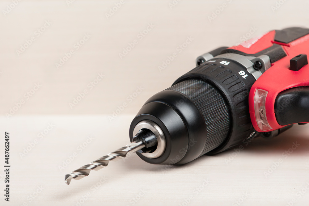 Cordless drill in black and red. A screwdriver with a drill lies on a wooden background. Modern carpentry tool close-up.