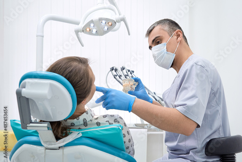 An orthodontist conducts a consultation on dental prosthetics. Doctor dentist shows an artificial plastic jaw with dental implants. Background of modern clinic