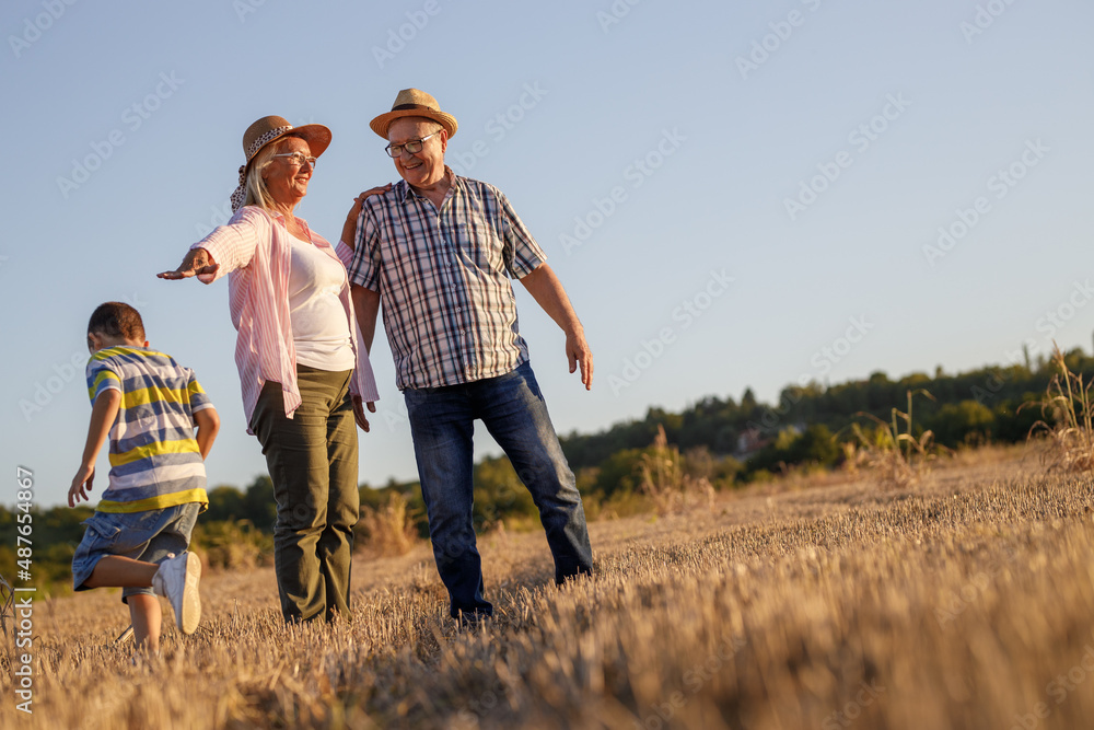 Grandparents with the grandson. They're playing on the meadow and joying in sunset.		