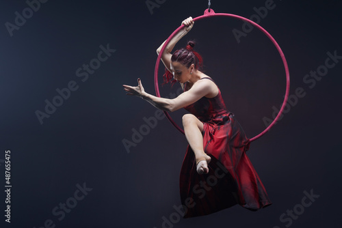 Circus performer woman in red dress doing tricks on red Lyra isolated on black background. photo