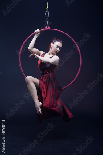 Circus performer woman in red dress doing tricks on red Lyra isolated on black background. © Naz