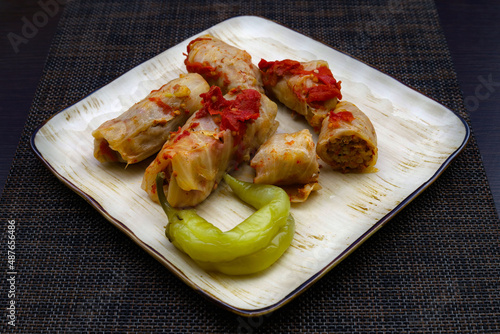 Traditional Caucasian dish Tolma or Dolma. Stuffed cabbage leaves with meat and rice and pickled green peppers in a plate on a dark background. Close-up photo