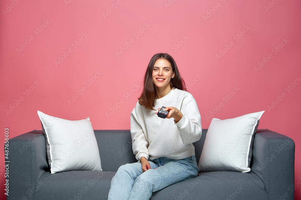 Smiling girl holding tv remote controller, sitting on couch, watching movie, spending leisure time with television Smiling girl holding tv remote controller, sitting on couch, watching movie, spending leisure time with television
