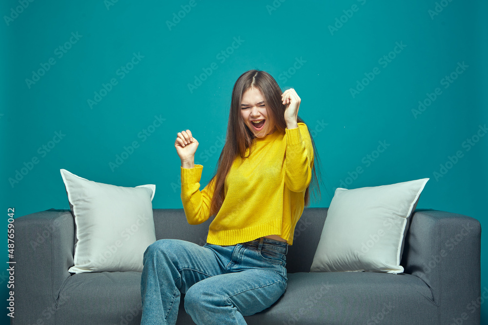 Dancing joyful young girl move in win dance having fun, enjoying music, celebrate success, sitting on sofa Dancing joyful young girl move in win dance having fun, enjoying music, celebrate success, sitting on sofa