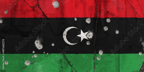 Full frame photo of a weathered flag of Libya painted on a cracked wall with bullet holes. Libyan Crisis, conflict and civil war concept. photo