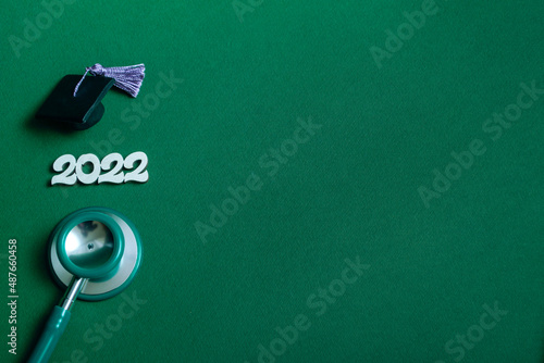 Graduation cap with stethoscope and numbers 2022 on green background, closeup with copy space. Medical education concept. © Tasha
