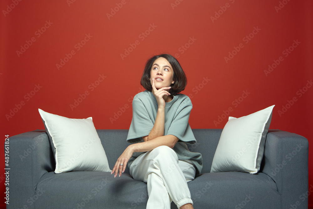 Thoughtful young beautiful girl dreaming sitting on sofa. Pensive woman touching chin looking up, contemplating Thoughtful young beautiful girl dreaming sitting on sofa. Pensive woman touching chin looking up, contemplating