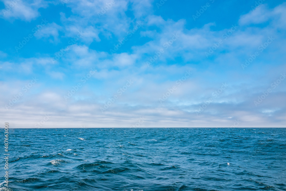 Colorful blue Pacific Ocean and partly cloudy sky background with copy space.