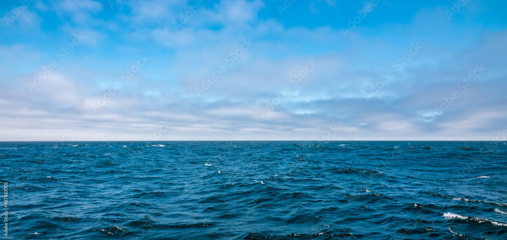 Obraz premium Colorful blue Pacific Ocean and partly cloudy sky background with copy space.