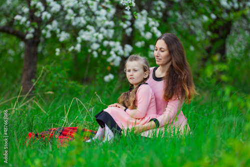 mother and daughter sit in the apple orchard in spring