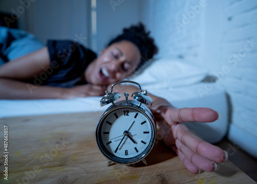 Attractive woman staring at alarm clock trying to sleep feeling stressed depressed and sleepless