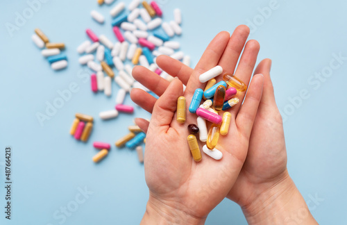 The girl holds in her hands a lot of multi-colored bright pills. Blue background, place for an inscription. Concepts of medicine and health.