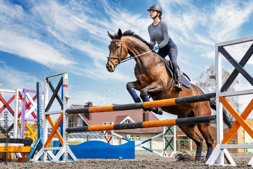 Equestrian sport. Show jumping competition. Young rider horseback girl jumping over an obstacle on her course