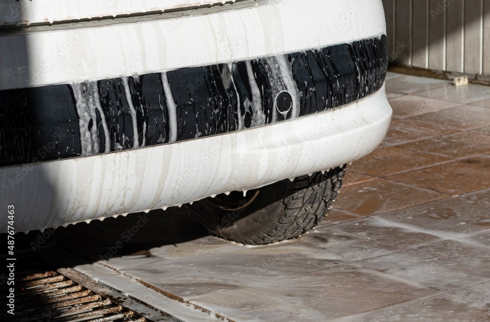 Car wash. White foam on rear bumper of white car in open garage Stock