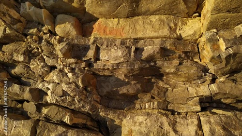 Cliff - rugged dipping sedimentary rock mountain formation. Vertical natural rough wall of stratum layers, jagged, sliced and cracked. Geological strata canyon - orange, brown and yellow.
