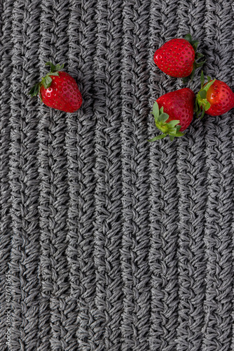 Four perfect shiny strawberries at the top part of a gray knitting cloth.