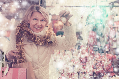 Portrait of happy mature woman in tinsel with Christmas toys at fair outdoor. © JackF
