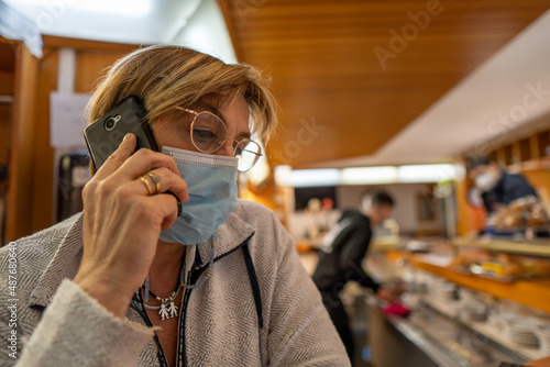 Old woman with mask and glasses calling on the phone in a bar