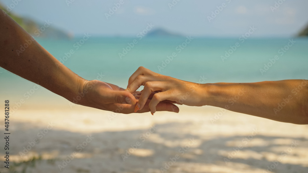 Hands of flirting young man and woman touching on beach in palms shadow against calm azure ocean close view. Traveling to tropical countries Hands of flirting young man and woman touching on beach in palms shadow against calm azure ocean close view. Traveling to tropical countries