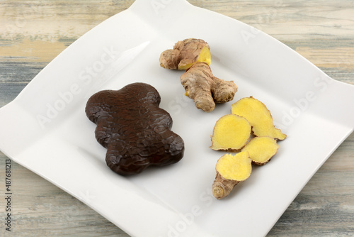 Chocolate covered Pryanik or pierniczki gingerbread cookie with fresh ginger on white snack plate photo