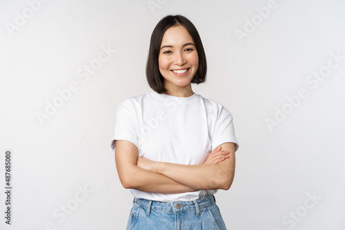 Portrait of happy asian woman smiling, posing confident, cross arms on chest, standing against studio background photo