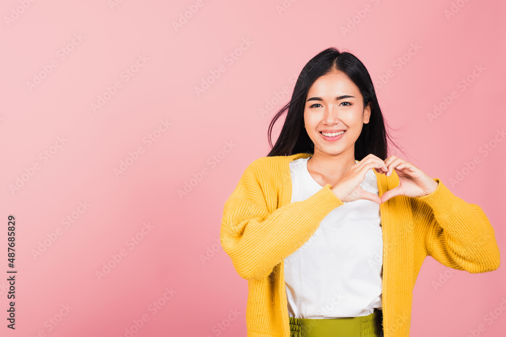 Happy Asian portrait beautiful cute young woman smile make finger heart gesture figure symbol shape sign with two hands sending love to her lover looking camera, studio shot isolated pink background Happy Asian portrait beautiful cute young woman smile make finger heart gesture figure symbol shape sign with two hands sending love to her lover looking camera, studio shot isolated pink background